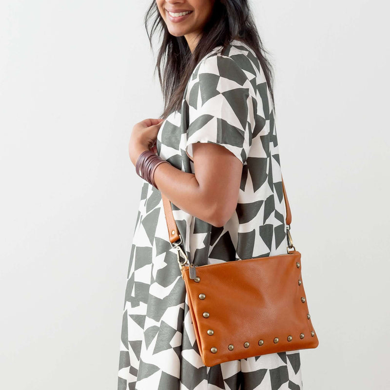 Woman wearing rust studded bag convertible as a small crossbody bag in studio