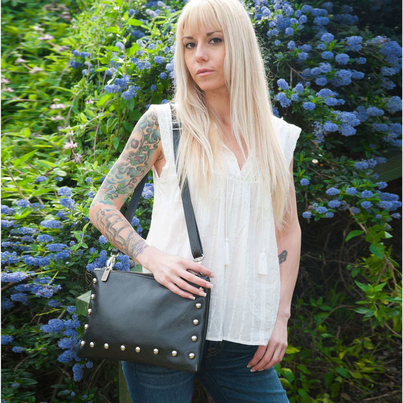 Woman wearing dark charcoal studded bag in full-grain leather as a small crossbody bag in the park
