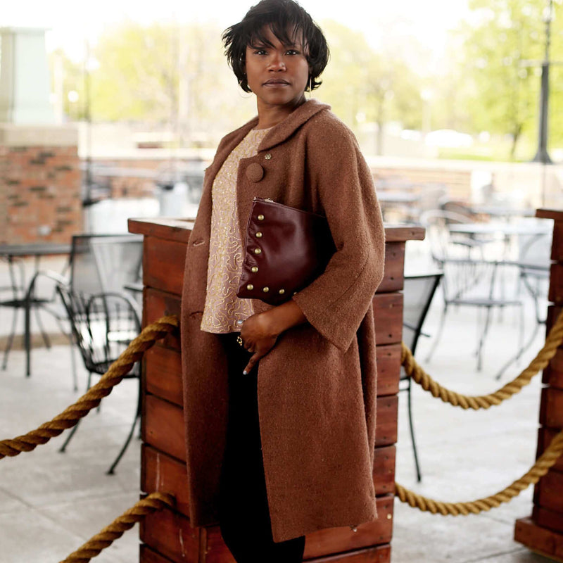 Woman wearing plum studded bag in full-grain leather as a clutch in city restaurant
