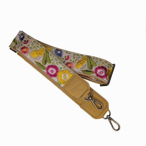 Floral embroidered strap with yellow leather end and metal hook on a white background
