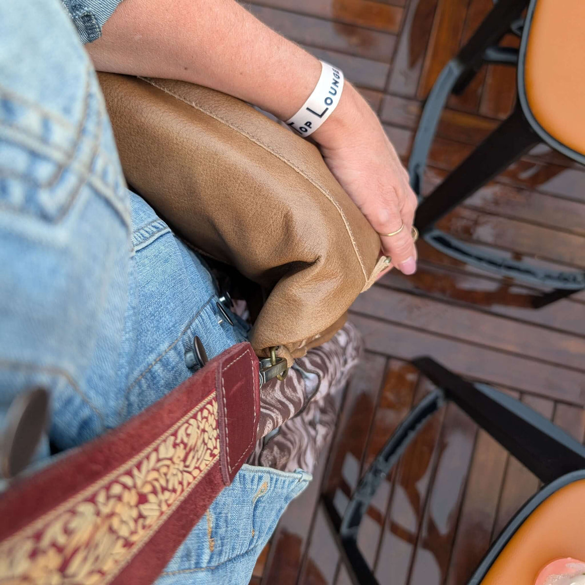 Designer Brynn Capella wearing a guitar bag strap featuring maroon floral design and leather trim with her Mini Lauren Rosarito Beach bag, sitting on a wooden deck.